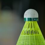 Close-up of a green plastic badminton shuttlecock with a white rubber tip against a blurred background.