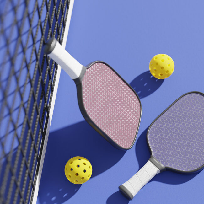 Two pickleball paddles and two yellow balls on a blue court near a black net.