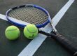 Two tennis balls and a tennis racquet lying on a court near white boundary lines.