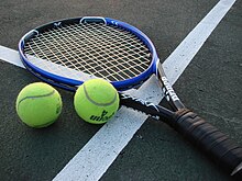 Two tennis balls and a tennis racquet lying on a court near white boundary lines.
